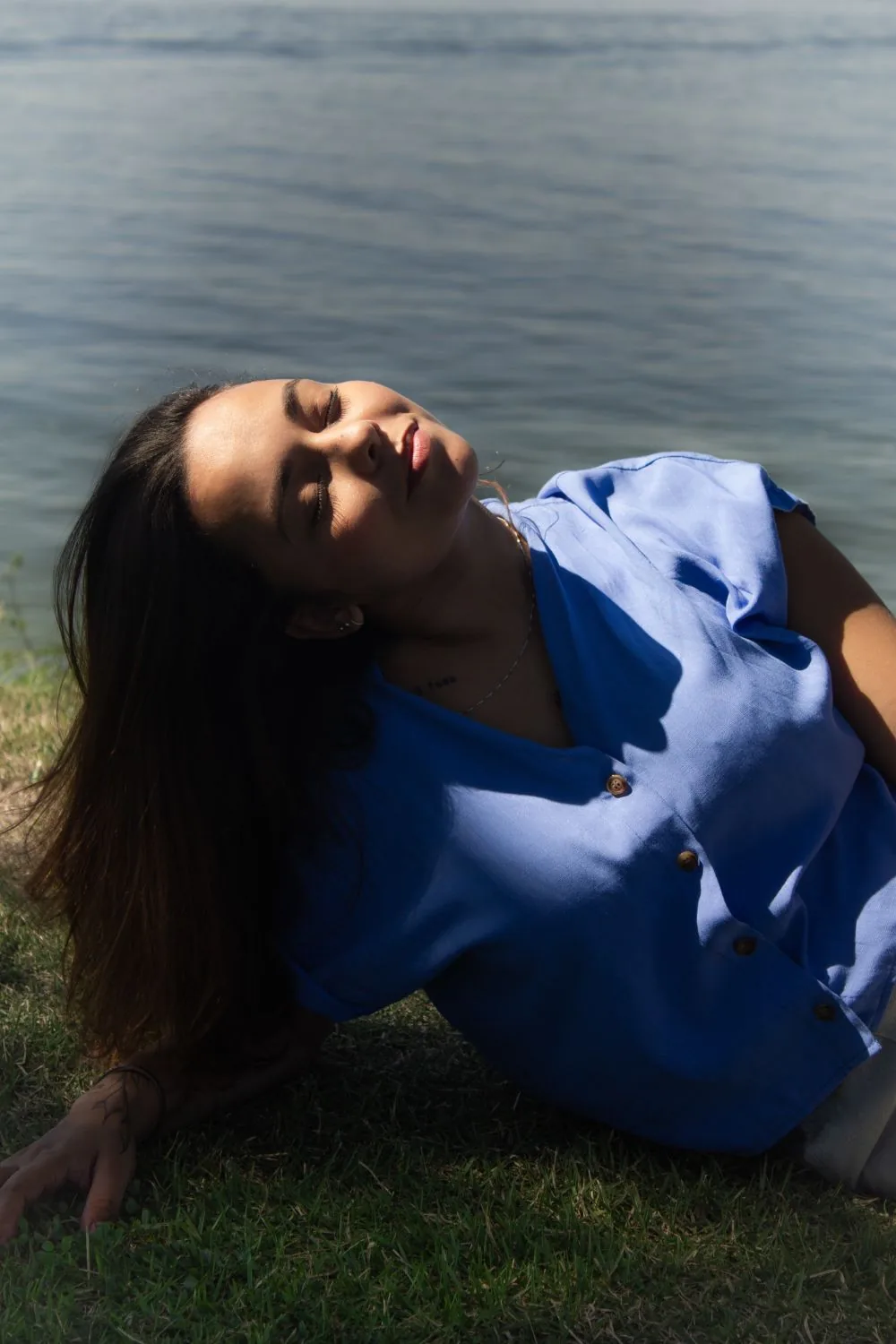 Deitada na grama de camisa azul, água ao fundo