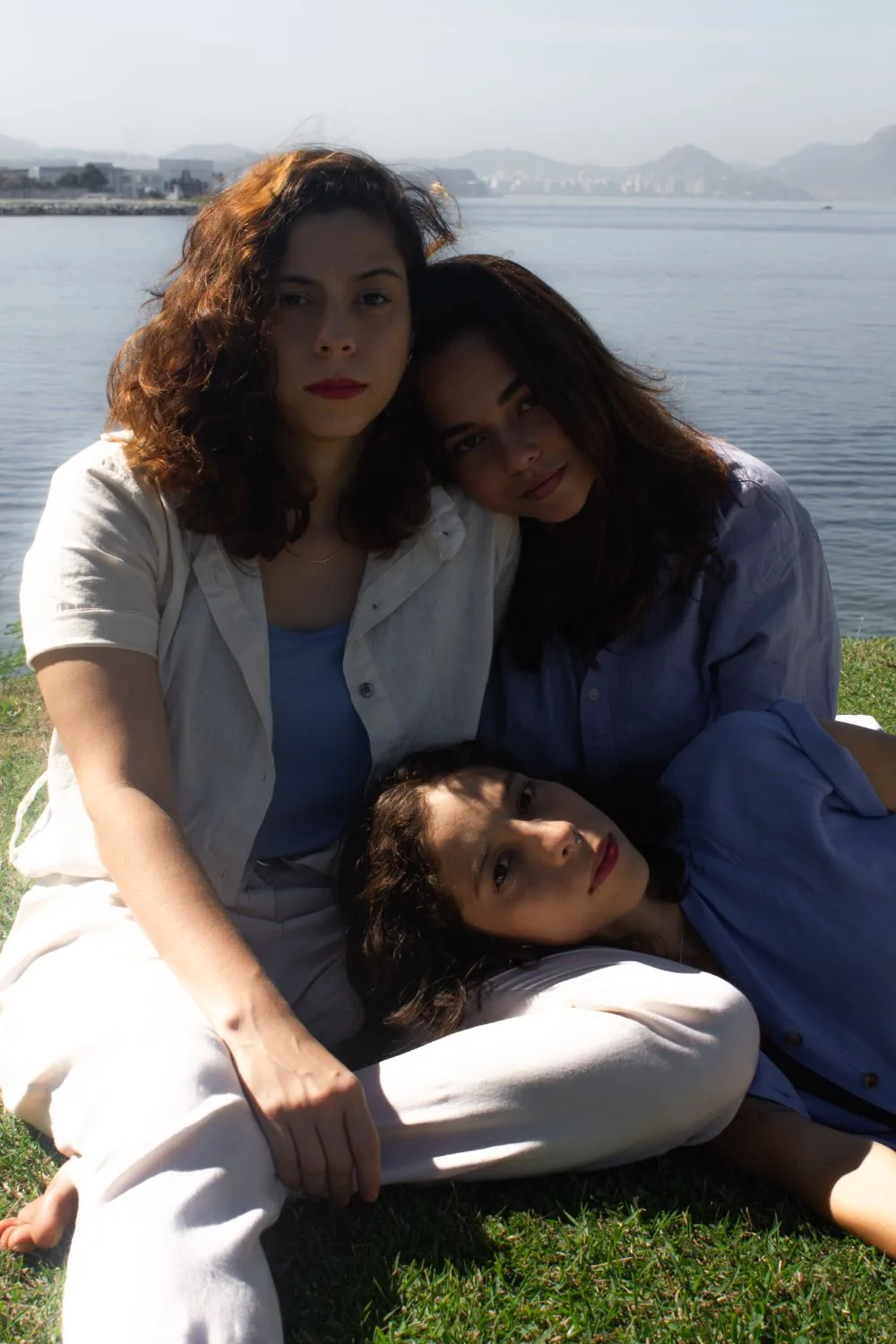 As três sentadas na grama, baía e morros ao fundo