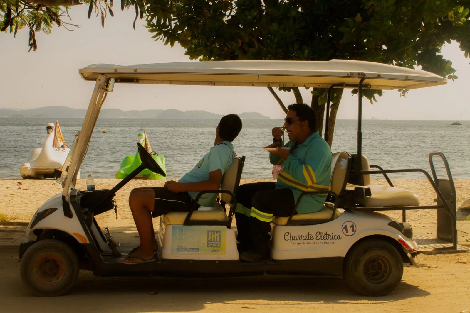 Charrete elétrica parada na areia, dois homens almoçando